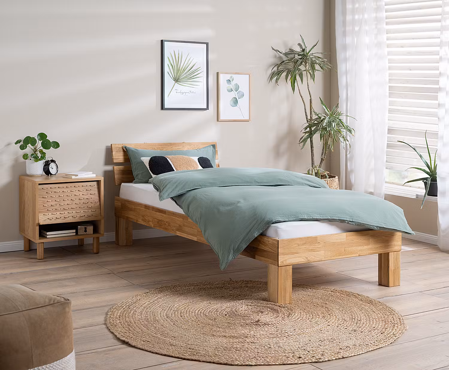 Einzelbett aus Massivholz im Naturstil mit passendem Nachttisch, dazu salbeigrüne Bettwäsche.