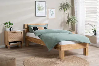 Einzelbett aus Massivholz im Naturstil mit passendem Nachttisch, dazu salbeigrüne Bettwäsche.