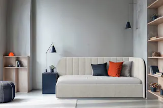 Hellgraues Schlafsofa mit bunten Kissen, dazu stylishe Leuchten im Industrial-Retro-Design..