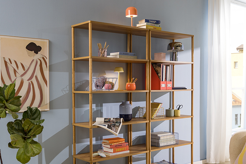 Modernes Standregal aus Holz vor himmelblauer Wand, dekoriert mit Körben, Büchern und Deko, dazu ein Holzregal mit Büchern und Schreibartikeln.