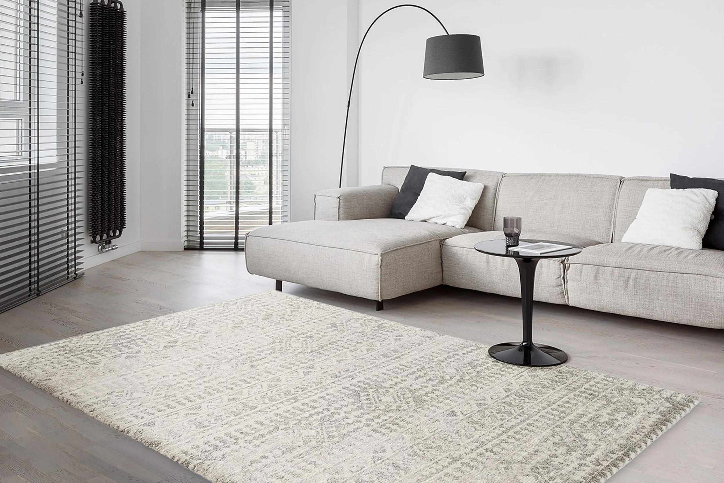 Grau gemusterter Teppich in minimalistischem Wohnzimmer mit hellgrauem Sofa und schwarzer Bogenlampe sowie Beistelltisch