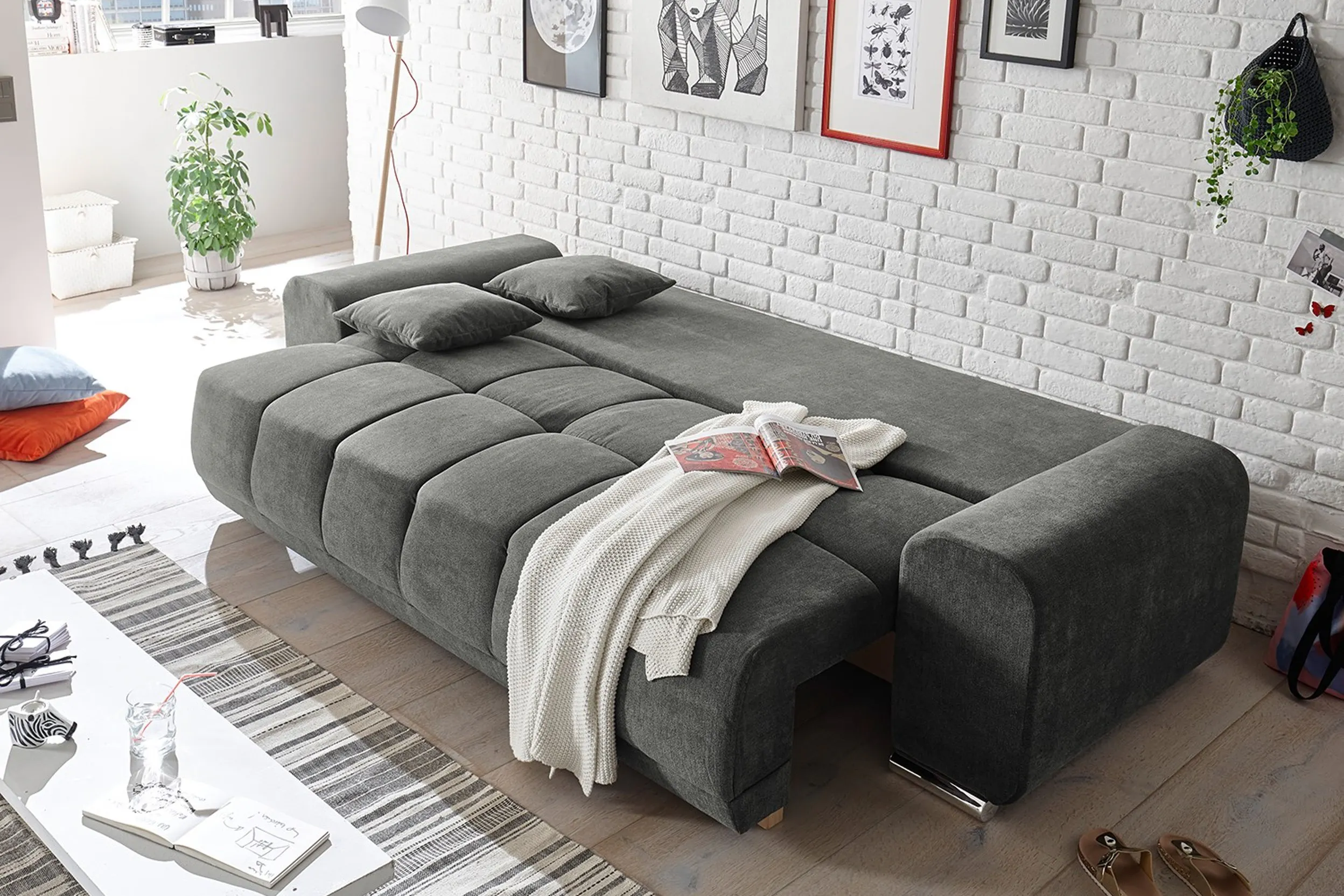 Ausgeklapptes Schlafsofa in Grau von weisser Backsteinwand