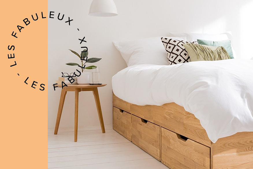 Lit en bois clair avec 3 tiroirs de rangement, linge de lit blanc et suspensions blanches au-dessus de la table de nuit en filigrane.