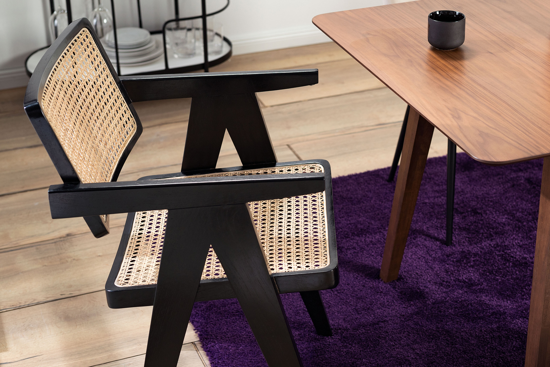 Chaise cannée devant une table de salle à manger en bois massif foncé, tapis violet et desserte noire. 