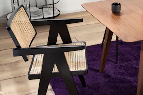 Chaise cannée devant une table de salle à manger en bois massif foncé, tapis violet et desserte noire.