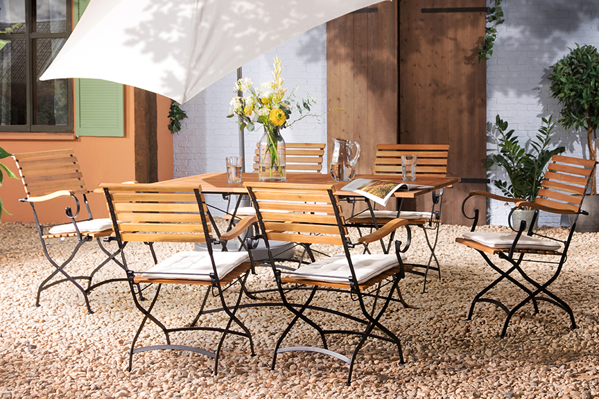 Terrasse mit Gartentisch, Gartenstühlen und Gartenbank aus Akazienholz mit hellblauen Sitzkissen, dazu ein weißer Sonnenschirm, ein gemusterter Outdoor-Teppich und Deko.