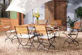 Terrasse mit Gartentisch, Gartenstühlen und Gartenbank aus Akazienholz mit hellblauen Sitzkissen, dazu ein weißer Sonnenschirm, ein gemusterter Outdoor-Teppich und Deko.