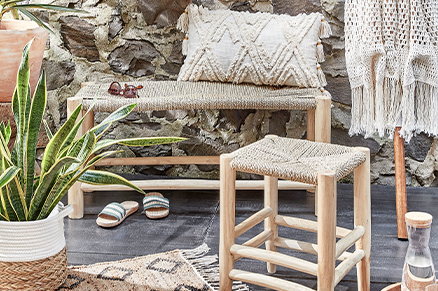 Holzbank und -hocker von BUTLERS mit beflochtener Sitzfläche sowie einem Juteteppich, beigen Boho-Kissen Bastkorb mit Grünpflanze; daneben Draufsicht auf einen Juteteppich, Kissen, Decke und Daybed in Beige sowie geöffnete Schälchen aus Bast.