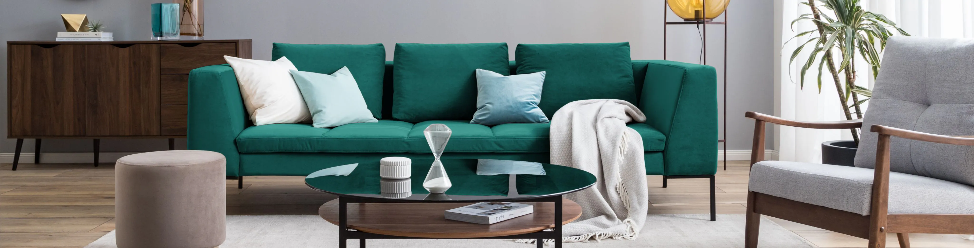 Grünes 3-Sitzer-Sofa in Wohnzimmer mit dunkelbrauner Kommode im Hintergrund sowie runder Couchtisch und Armlehnensessel