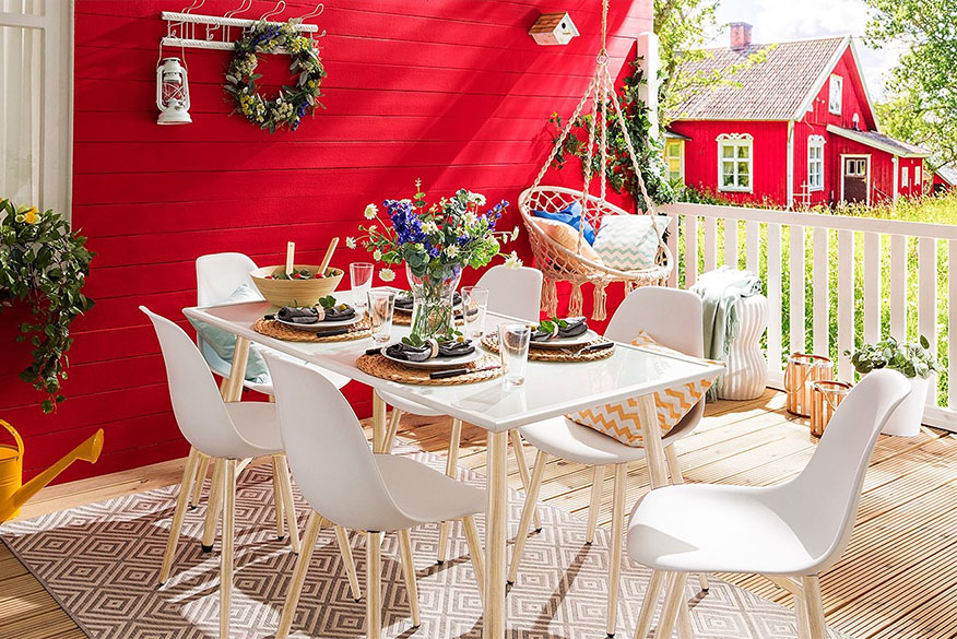 Weisse Gartenmöbel im Skandi-Stil vor typisch skandinavisch roter Hauswand und dekoriert mit urigen Accessoires wie einer Blechgiesskanne und Blumenkränzen im Midsommar-Look.