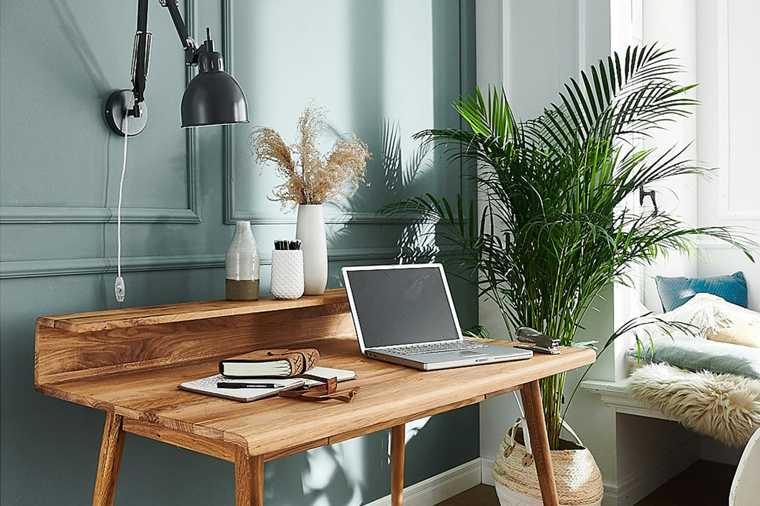Schreibtisch aus Massivholz mit Laptop und Notizbüchern vor einer grün-blauen Wand