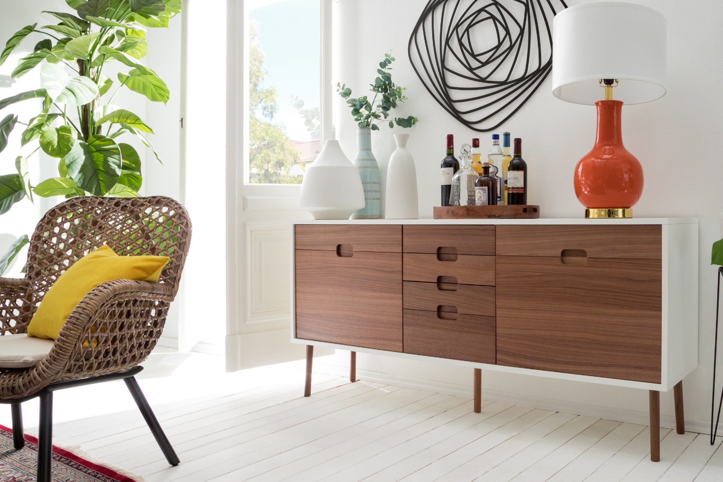 Stilvoller Einrichtungsmix aus Holzkommode und geflochtener Sessel mit Deko