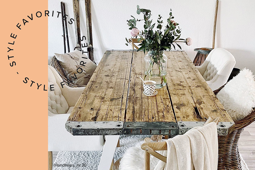 Esszimmer im Landhausstil mit Esstisch aus unbehandeltem, rauem Holz, Esszimmerstühlen aus dunklem Rattan sowie weißen Stühlen mit Chesterfield-Knöpfung; daneben Esstisch mit Holzplatte sowie graue Polsterstühle im Skandi-Stil.