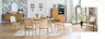 Heller Holztisch mit sechs Esszimmerstühlen mit Wiener Geflecht in einem Altbau-Esszimmer mit Holzboden, weißen Wänden, Kugellampen und Kommoden im Hintergrund, wobei die linke vor einer schwarz-weiß marmorierten Tapete steht; ein Holzstuhl mit Wiener Geflecht wird als Statement Chair in Szene gesetzt.