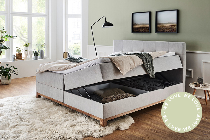 Hellgraues Polsterbett mit zwei Bettkästen für mehr Stauraum im Schlafzimmer, welches vor mintgrüner Wand auf einem Holzfußboden steht; daneben Innenansicht eines mit Kissen und Decken gefüllten Bettkastens.