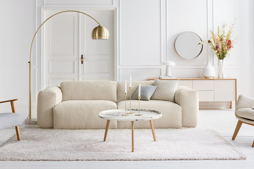 Salon dans les tons blancs et crème avec lampadaire et suspension dorés, tapis beige, canapé et repose-pieds en bouclette blanc crème ; à côté, gros plan sur un capitonnage en bouclette crème