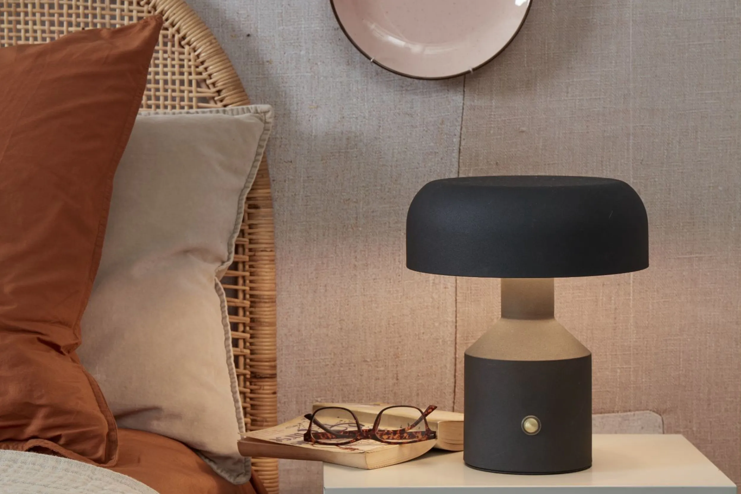 Schwarze Nachttischlampe neben einem Rattanbett mit rostoranger Bettwäsche