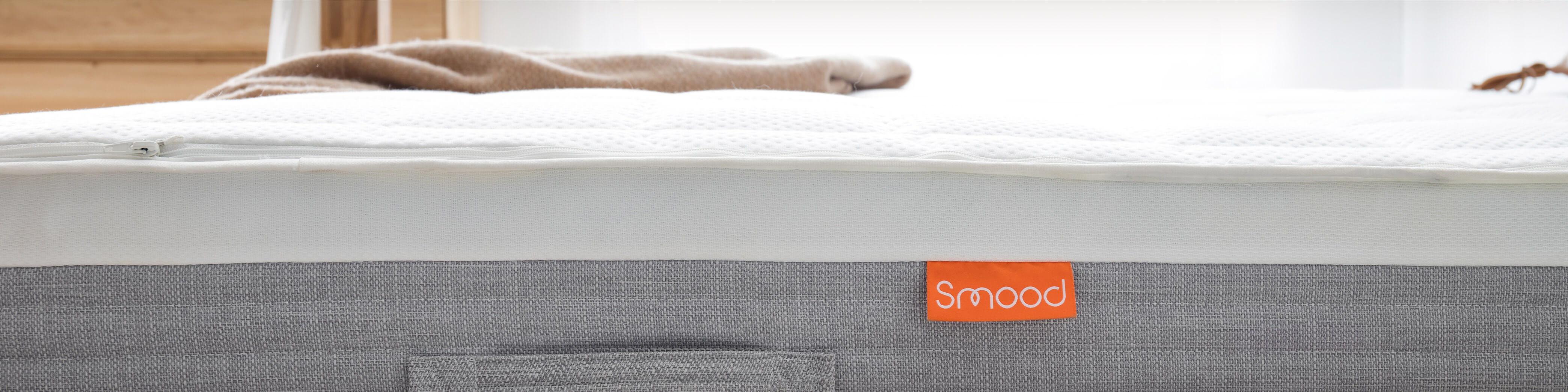Seitenansicht einer hellgrauen Matratze mit orangenem Smood-Etikett 