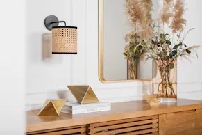 Buffet en bois avec bouquet de fleurs séchées, miroir cerclé de doré et objets déco dorés.