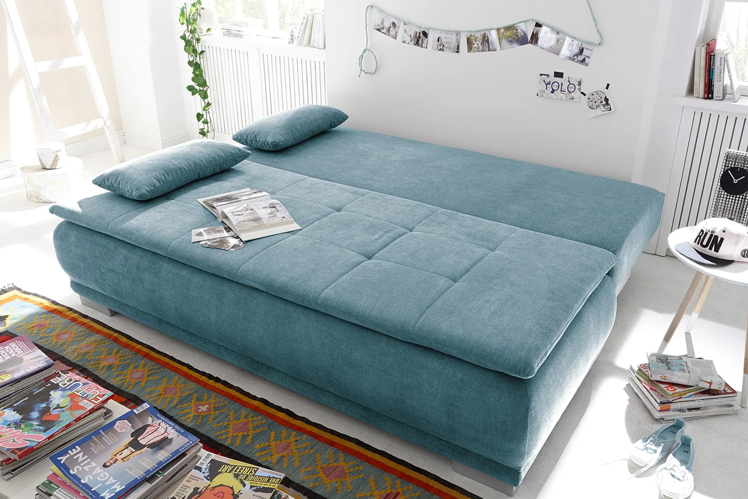 Hellblaues Schlafsofa im ausgeklappten Zustand in einem Jugendzimmer mit Fotos und Zeitschriften
