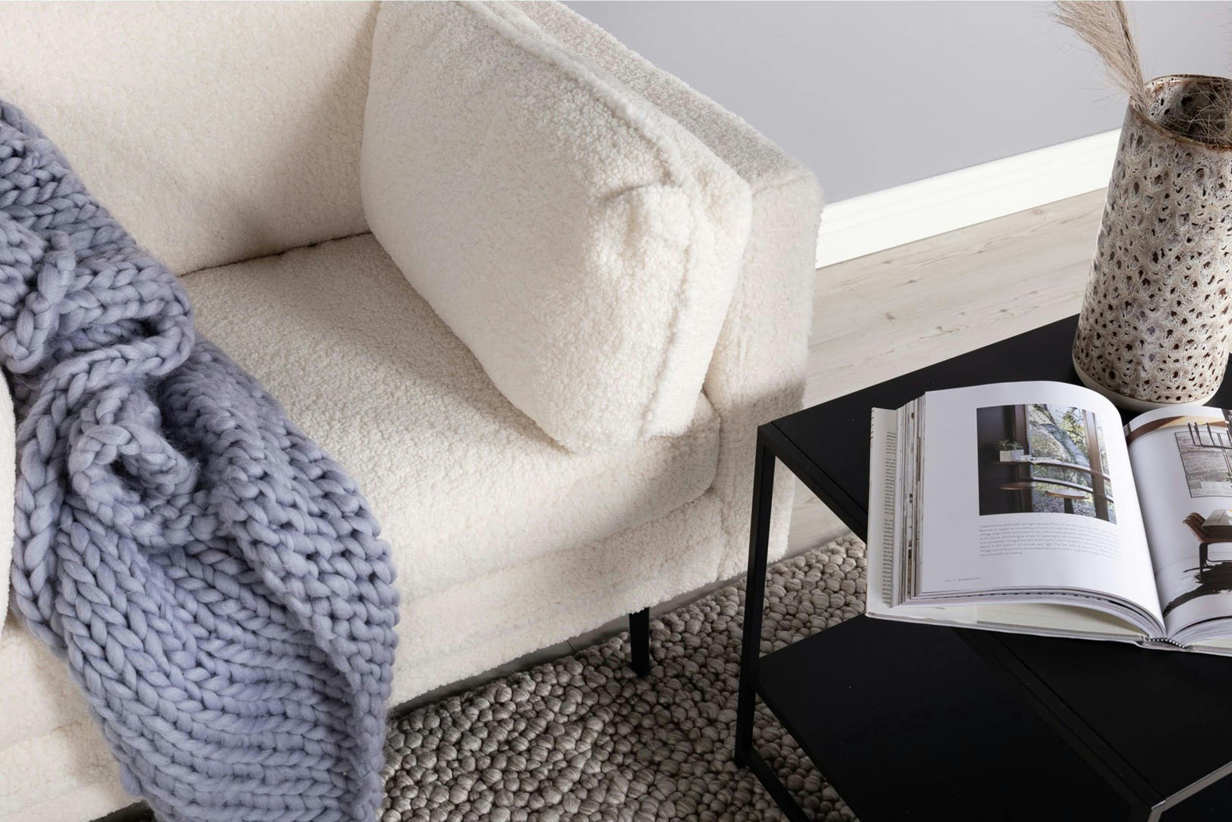 Nahaufname einer Armlehne mit Kissen hinter einem schwarzen Tisch mit Vase und Magazin