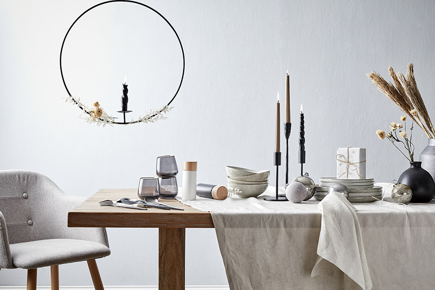 Minimalistische Weihnachtsdeko vor hellem Hintergrund: schwarzweißes kuscheliges Plaid, goldene Hirschfiguren, schwarzes kleines Windlicht, LED-Weihnachtsbaum in schlichter Dreiecksform sowie drei brennende Kerzen