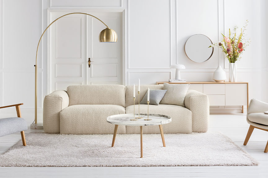 Salon dans les tons blancs et crème avec lampadaire et suspension dorés, tapis beige, canapé et repose-pieds en bouclette blanc crème ; à côté, gros plan sur un capitonnage en bouclette crème