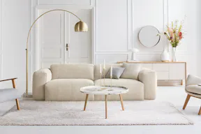 Salon dans les tons blancs et crème avec lampadaire et suspension dorés, tapis beige, canapé et repose-pieds en bouclette blanc crème ; à côté, gros plan sur un capitonnage en bouclette crème