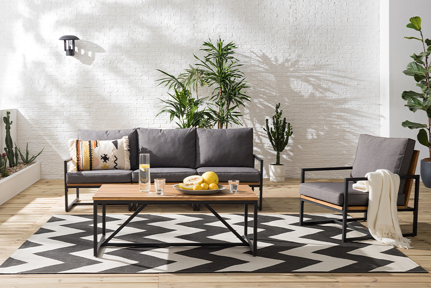 Gartenmöbel aus Holz und Metall im Industrial-Stil mit Textilien im Boho-Look, Pflanzen und Outdoorteppich.
