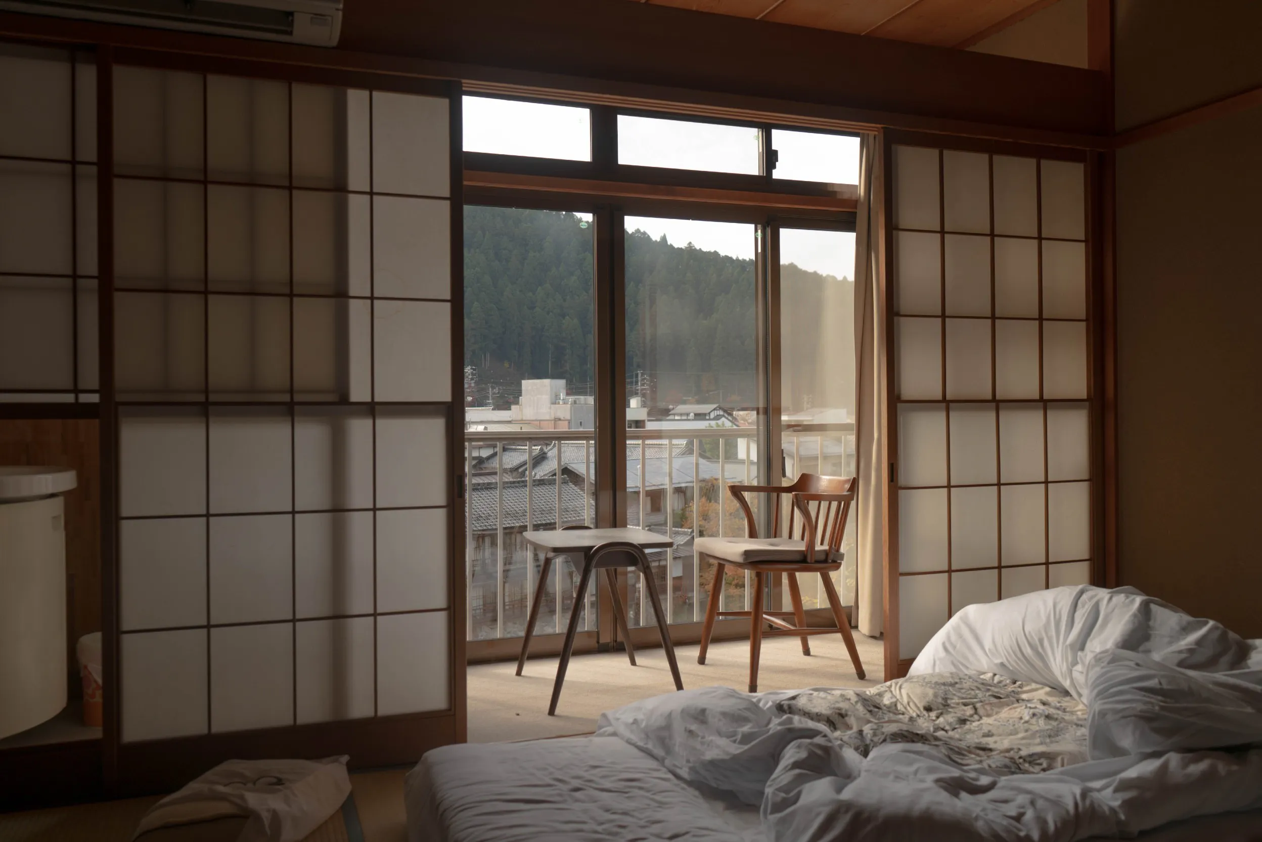 Schlafzimmer mit Bett, Stuhl vor grossem Fenster und Ausblick auf Stadt