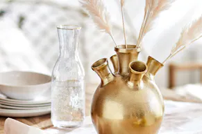 Vaisselle blanche et carafe à la bordure dorée, pot de fleurs et couverts dorés.