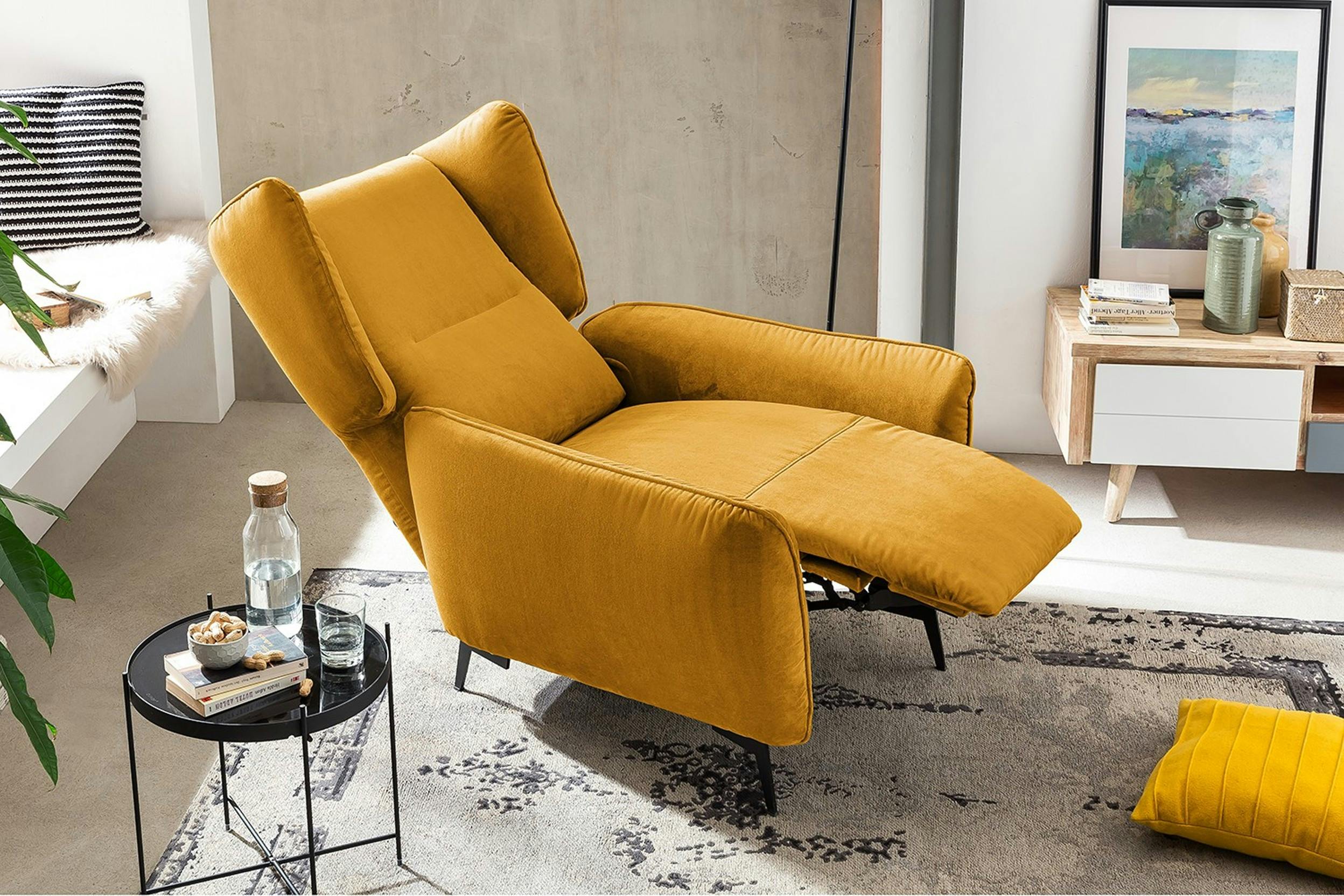 Ausgeklappter Relaxsessel in Gelb neben einem schwarzen Beistelltisch mit Snacks und Büchern