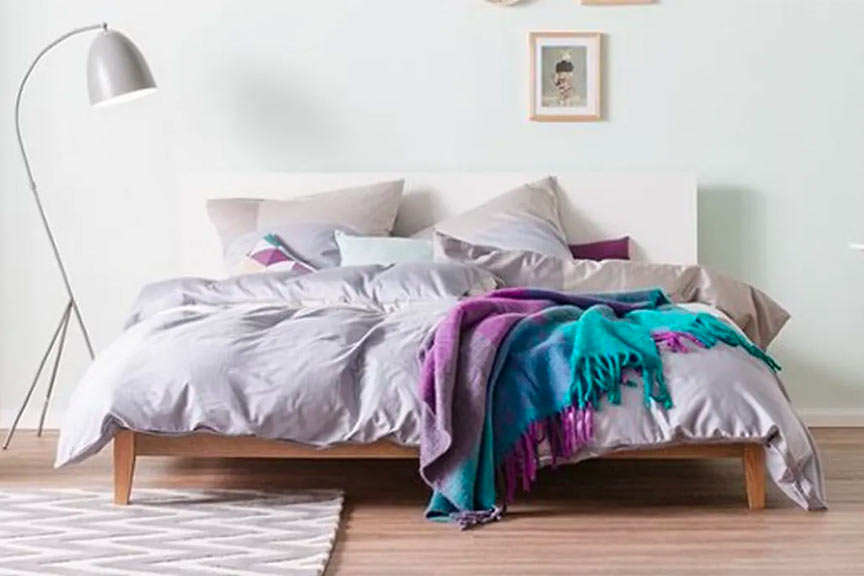 Bett aus Holz mit Decken und Bettbezügen, weiße Stehlampe