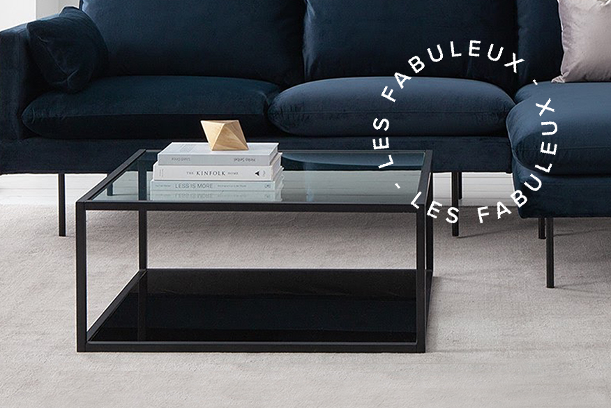 Table basse en métal noir et verre avec un canapé bleu et beige.