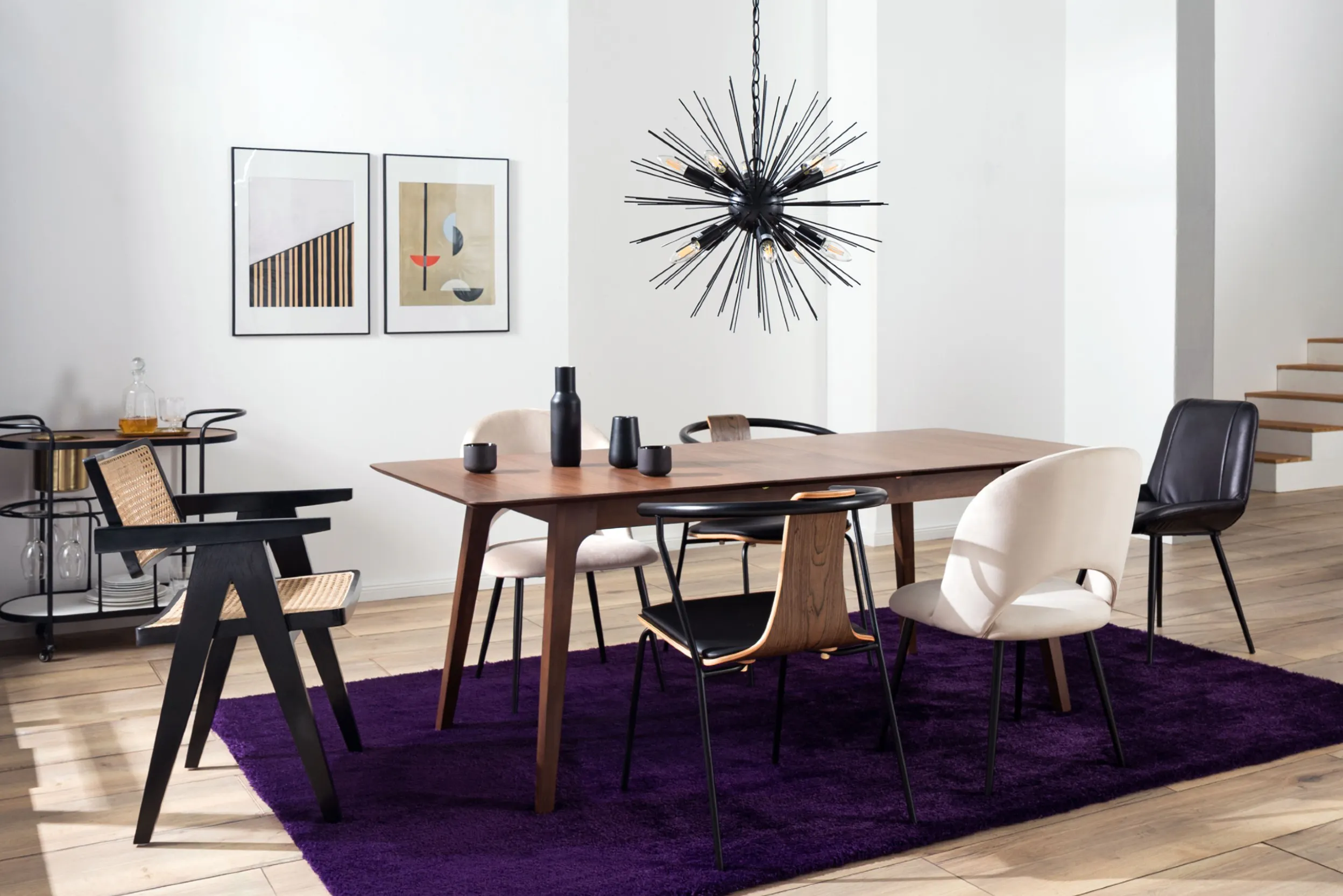Eklektisch angehauchtes Esszimmer mit Holztisch, lila Teppich und verschiedenen Stühlen und schwarzer Pendelleuchte