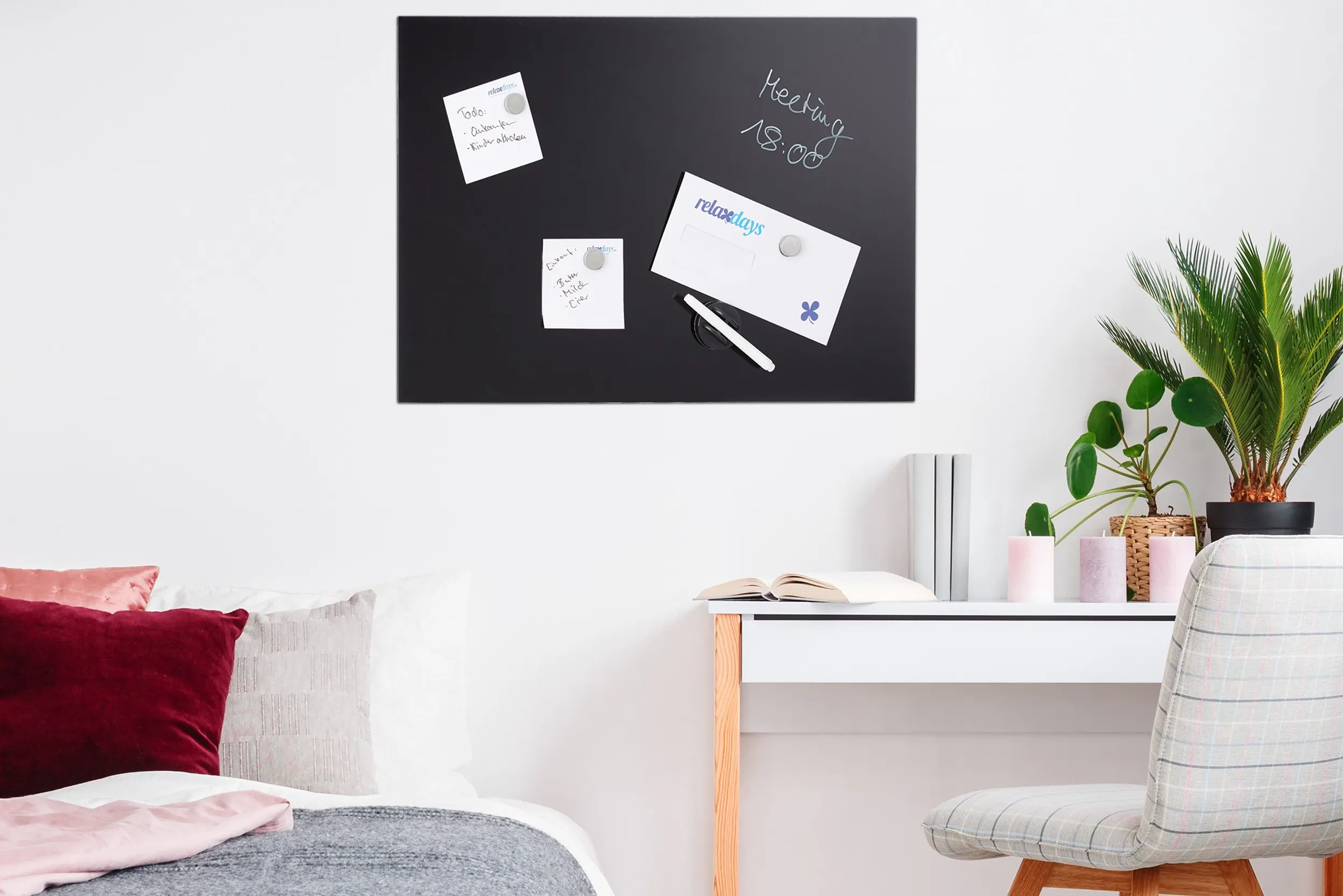 Schwarze Magnettafel mit verschiedenen Notizen über einem weißen Schreibtisch mit Holzelementen