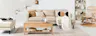 Wohnzimmer mit Möbeln der Serien Fort Dodge und Taylor der home24 Exklusivmarke kollected: Im Mittelpunkt ein beiges Sofa, dazu ein Couchtisch mit geflochtenen Applikationen, Pendelleuchten aus Rattan, Kissen, Teppich und Plaid in Beige- und Cremetönen sowie viele Dekoobjekte im Wandregal.