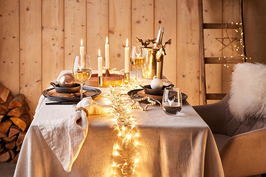 Bougeoir couronne de l'avent en bois et cerf décoratif doré sur une nappe en lin blanche, boules de Noël et étoiles.