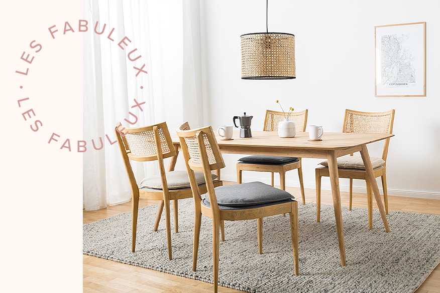 Salle à manger en bois blond avec table en chêne clair, chaises en rotin et frêne huilé et aux assises capitonnées, tapis en laine beige et lampe tressée. Gros plan sur du chêne clair.