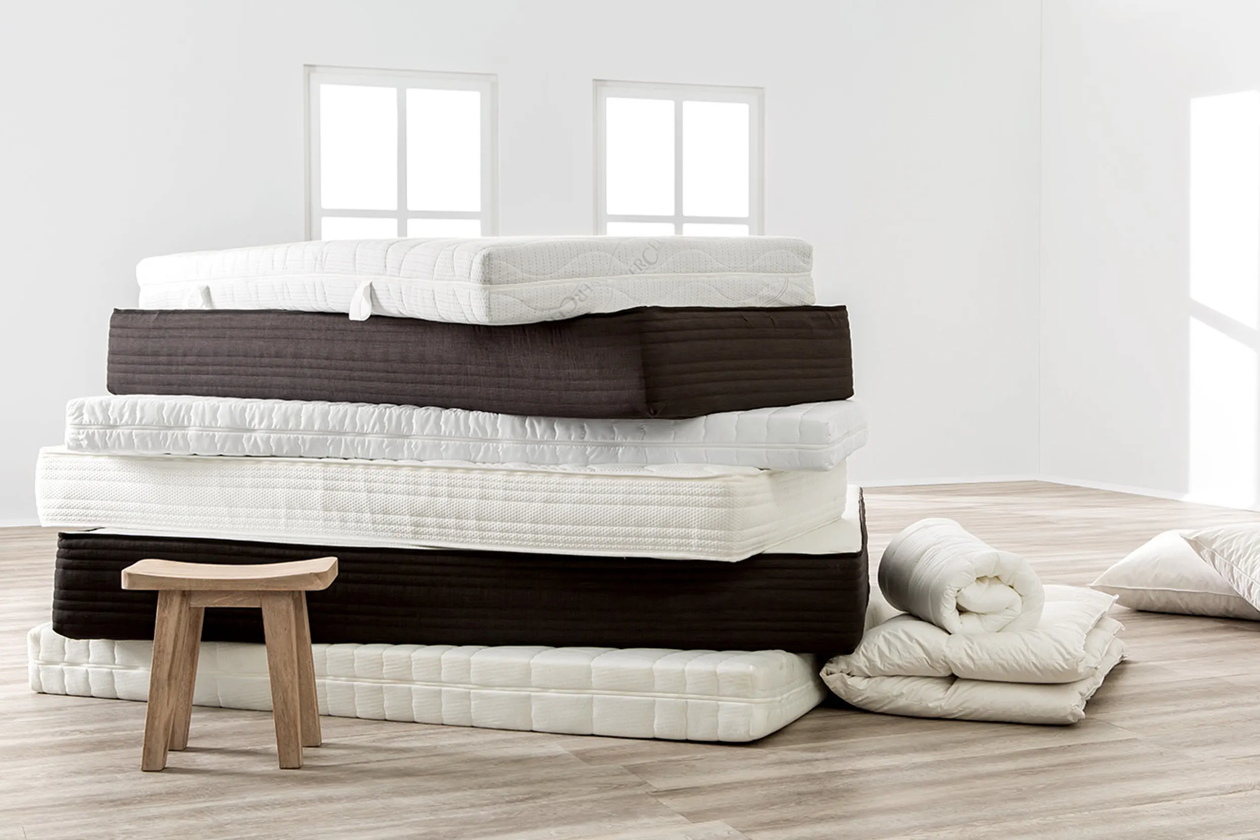 Ein Stapel mit 6 verschiedenen Matratzen hinter einem Holzhocker