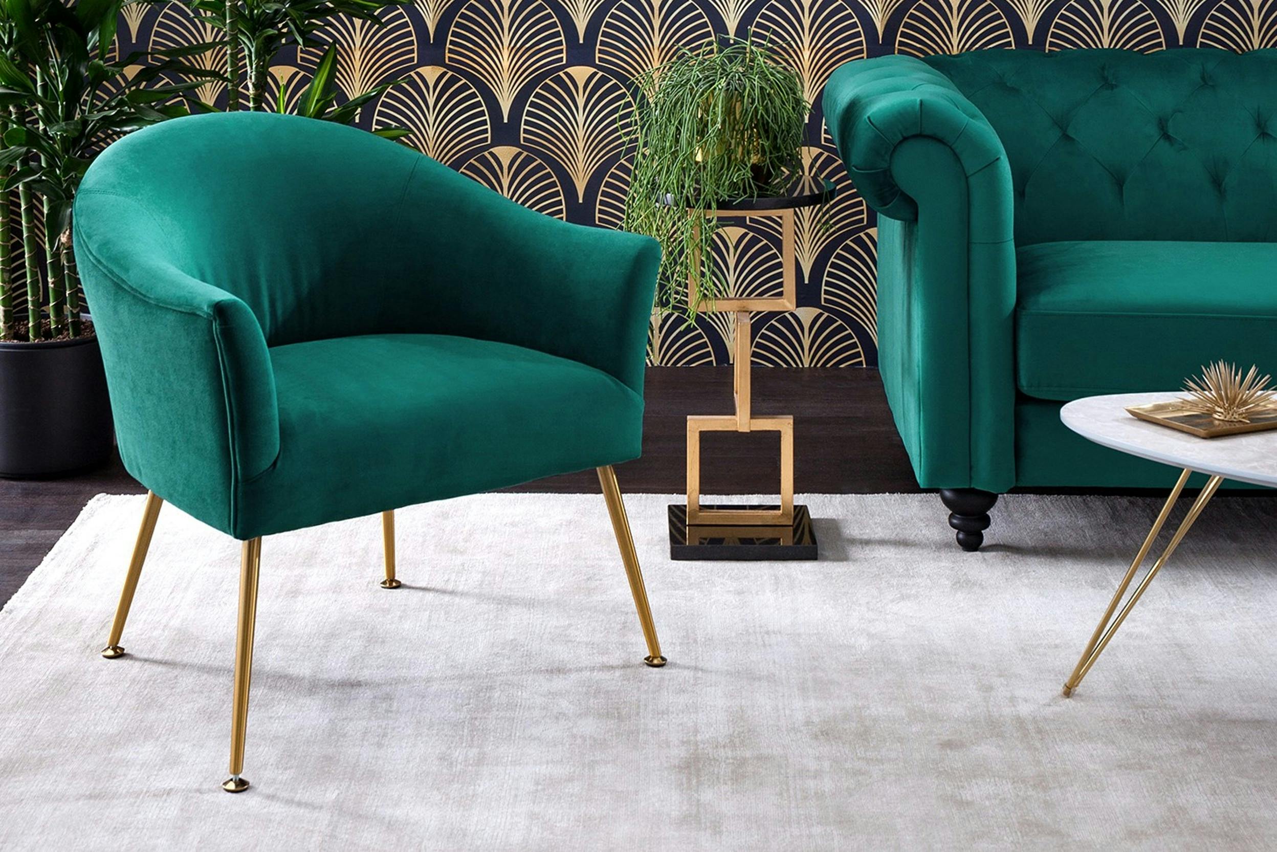 Petrolfarbener Samtsessel mit goldenen Metallfüßen vor einer gold-blau gemusterten Tapete
