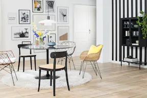 Esszimmer mit Rattan- und Holzstühlen sowie einem Glastisch in Marmoroptik. Dazu ein weißer Teppich, eine weiße Pendelleuchte, eine Bilderwand sowie ein schwarzes Highboard aus Metall vor einer schwarz-weißen Streifentapete.