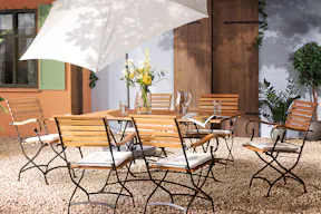 Terrasse mit Gartentisch, Gartenstühlen und Gartenbank aus Akazienholz mit hellblauen Sitzkissen, dazu ein weisser Sonnenschirm, ein gemusterter Outdoorteppich und Deko.