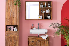 Badezimmer mit Badmöbeln der Serie Deva by kollected aus hochwertigem Sheeshamholz im Industrial-Stil, die vor einer rosafarbenen Wand stehen. Das Highboard wird mit einem roten Rundbogen dahinter noch mal farblich hervorgehoben.