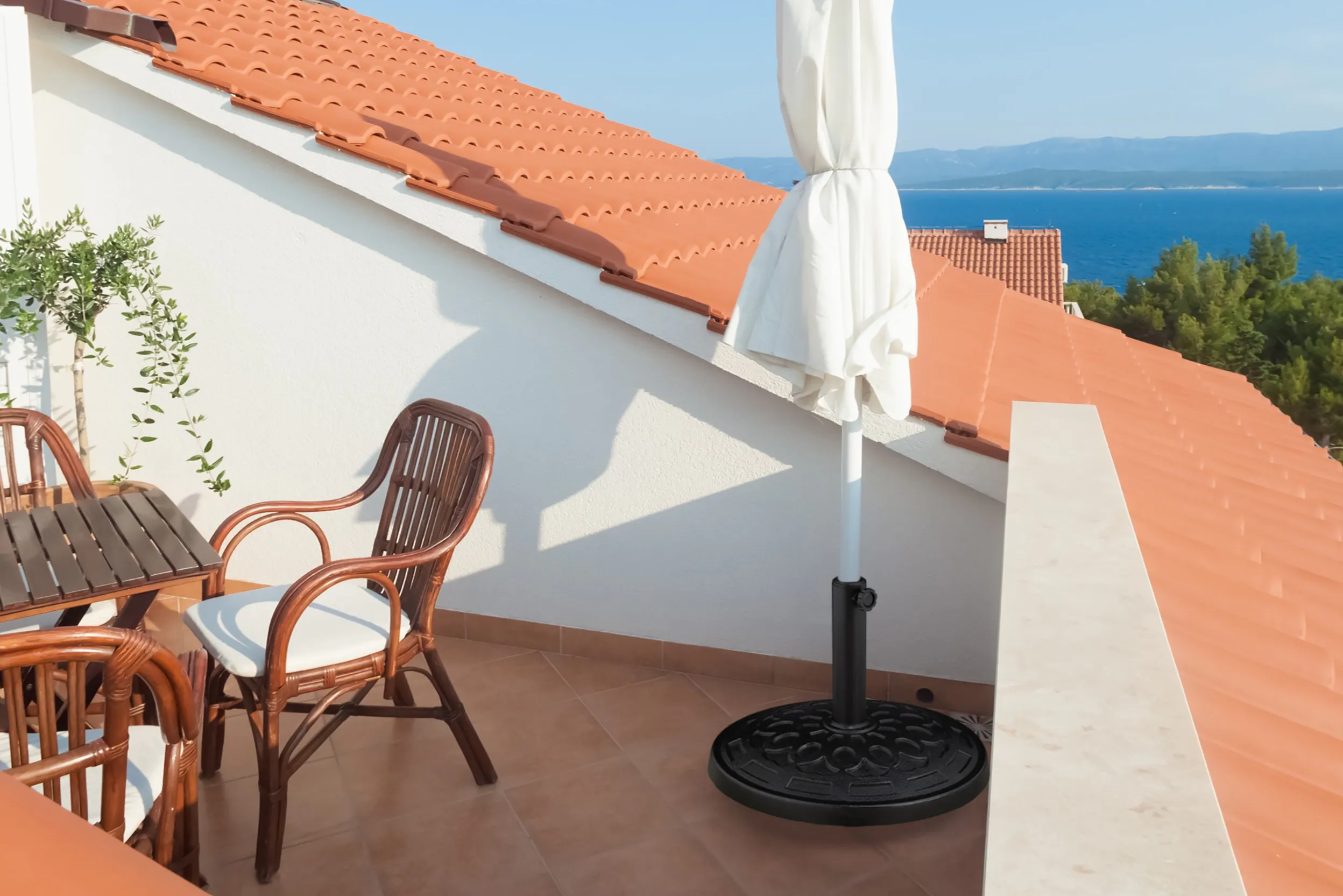Gefalteter weisser Sonnenschirm im Metallständer auf einer sonnigen Dachterrasse