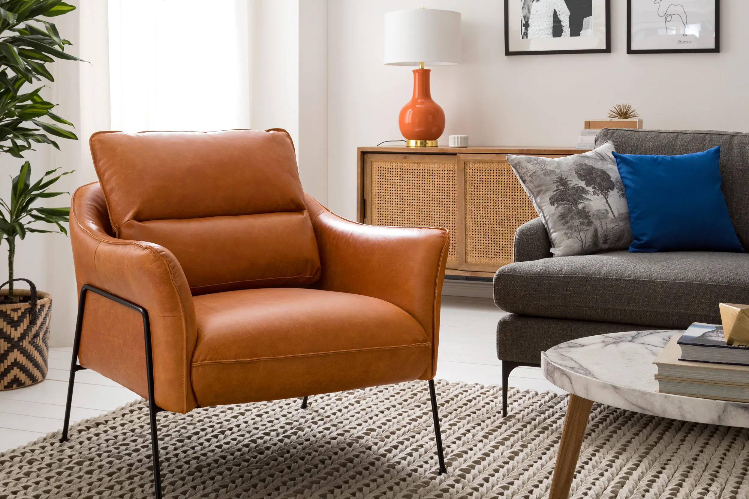 Brauner Ledersessel und Sofa aus Webstoff vor Kommode mit Wiener Geflecht