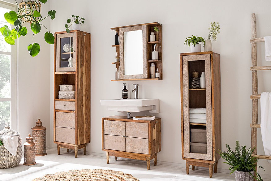 Meuble de salle de bain de style bohème en bois d'acacia avec des motifs de couleur crème, entourés de plantes vertes, de lanternes, de nombreux paniers de rangement et d'un tapis en jute.