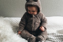 Baby sitzt auf einem Bett mit weißer Bettdecke und Kuscheldecke
