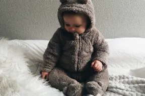 Baby sitzt auf einem Bett mit weißer Bettdecke und Kuscheldecke