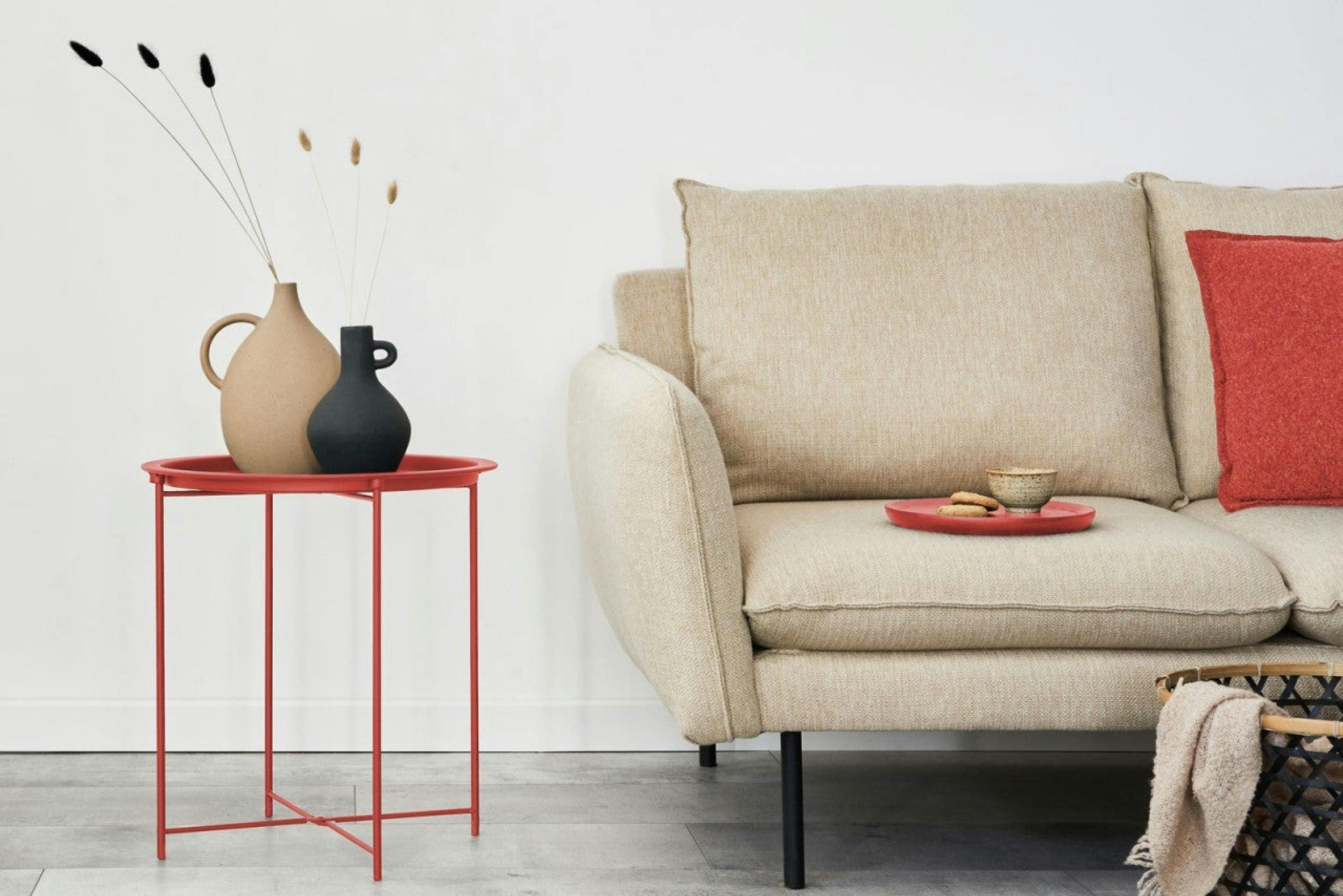 Roter Beistelltisch neben einem beigen Sofa mit rotem Kissen und rotem Tablett